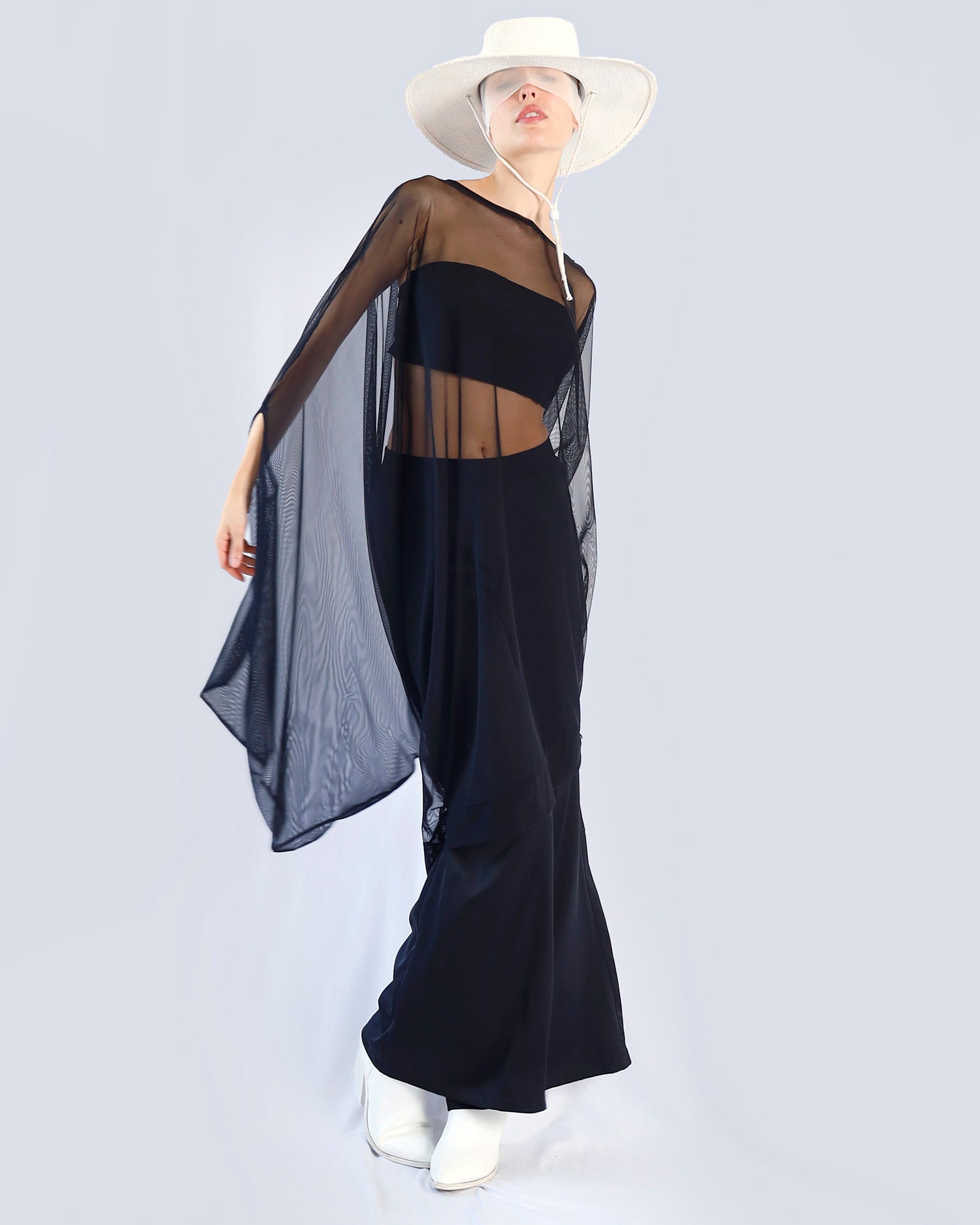 Person wearing a black outfit with sheer overlay and white hat on a light gray background. Maison Marie Saint Pierre | Dress | PHASMINA | Black | Pants | PAMELA | Black