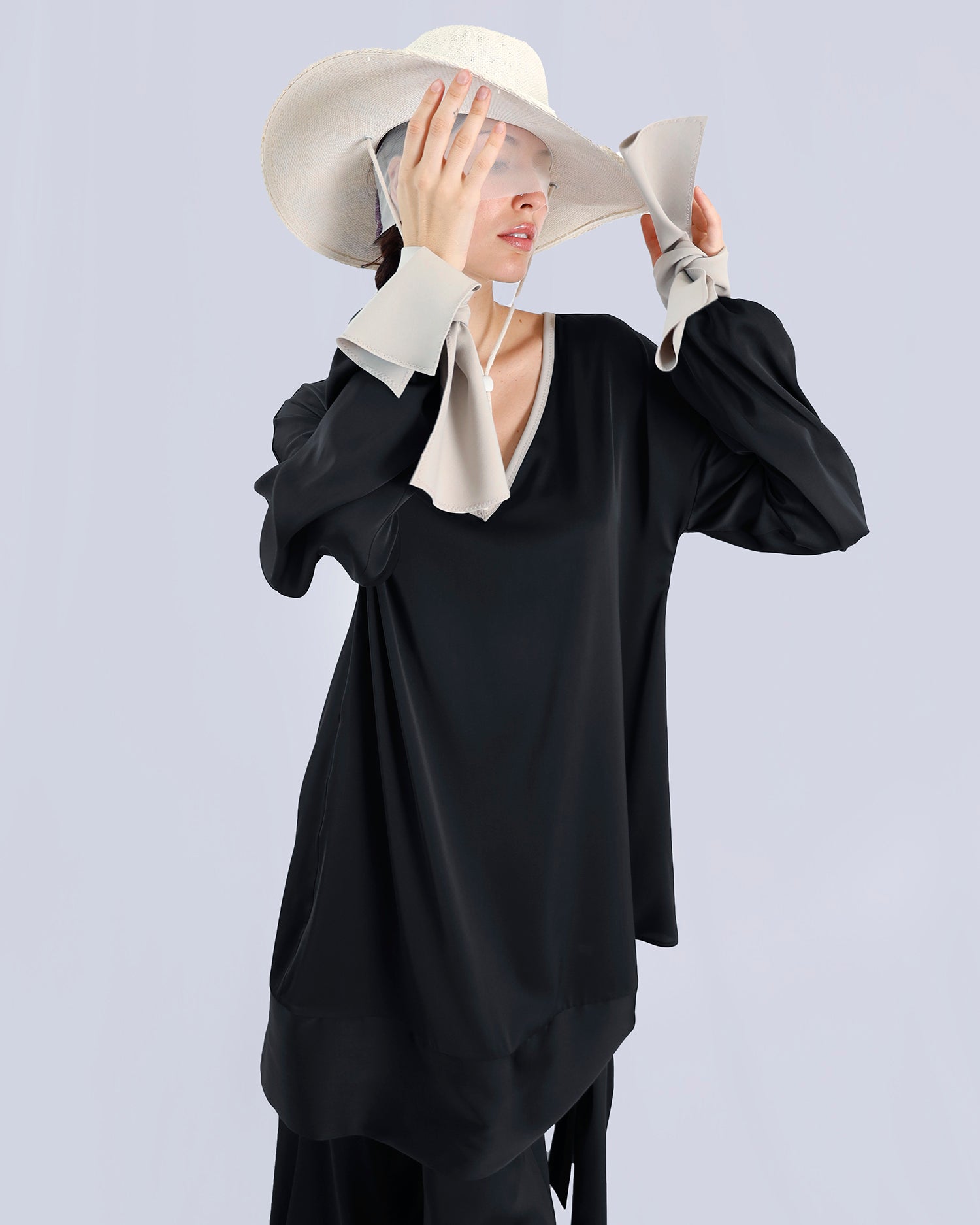 Person wearing a black outfit with a white hat and gloves on a light gray background. Maison Marie Saint Pierre | Tunique | PELLEGRINA | Black-Fog | Pants | PAMELA | Black 
