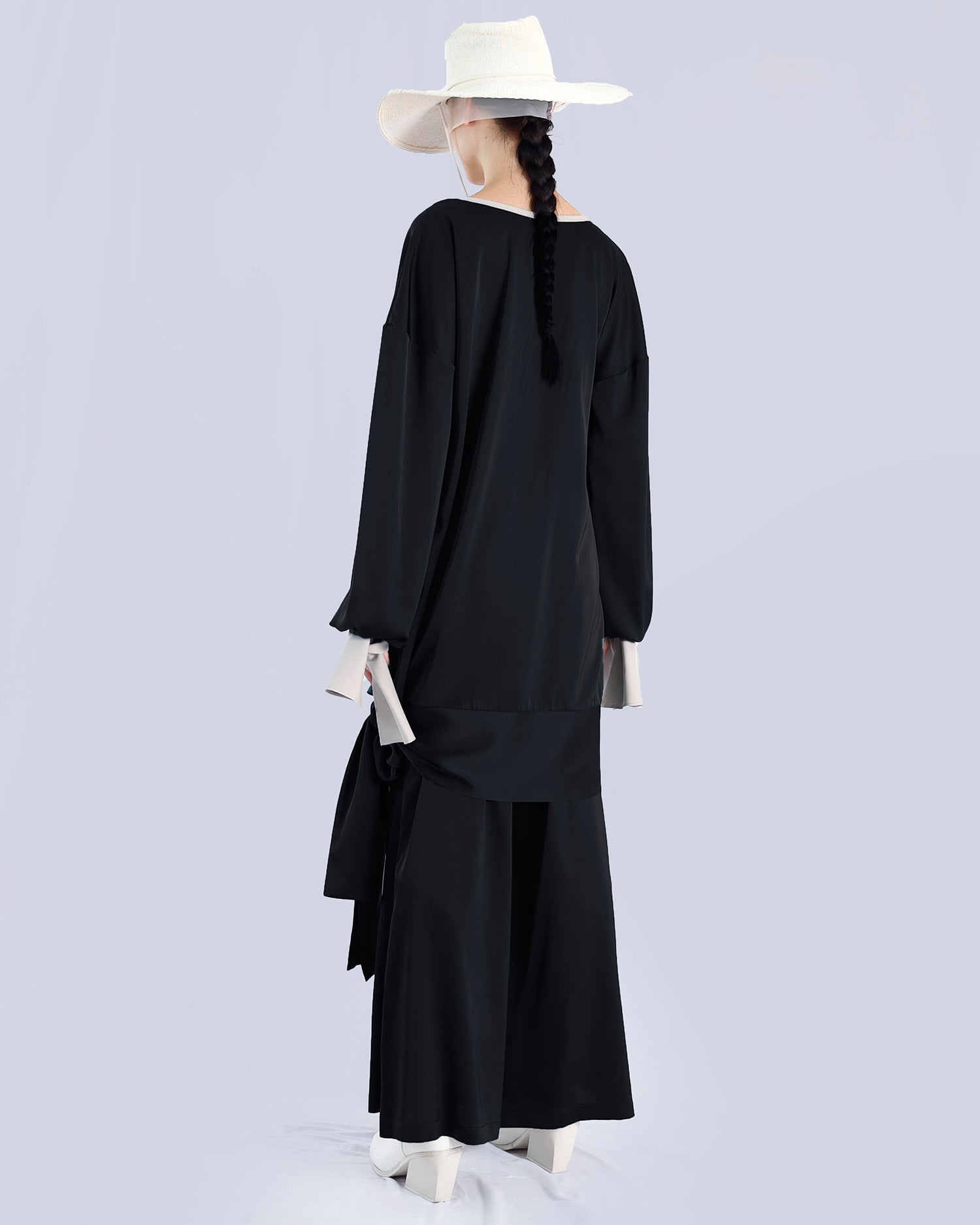 Person wearing a black outfit with a white hat on a light gray background. Maison Marie Saint Pierre | Tunique | PELLEGRINA | Black-Fog| Pants | PAMELA | Black 