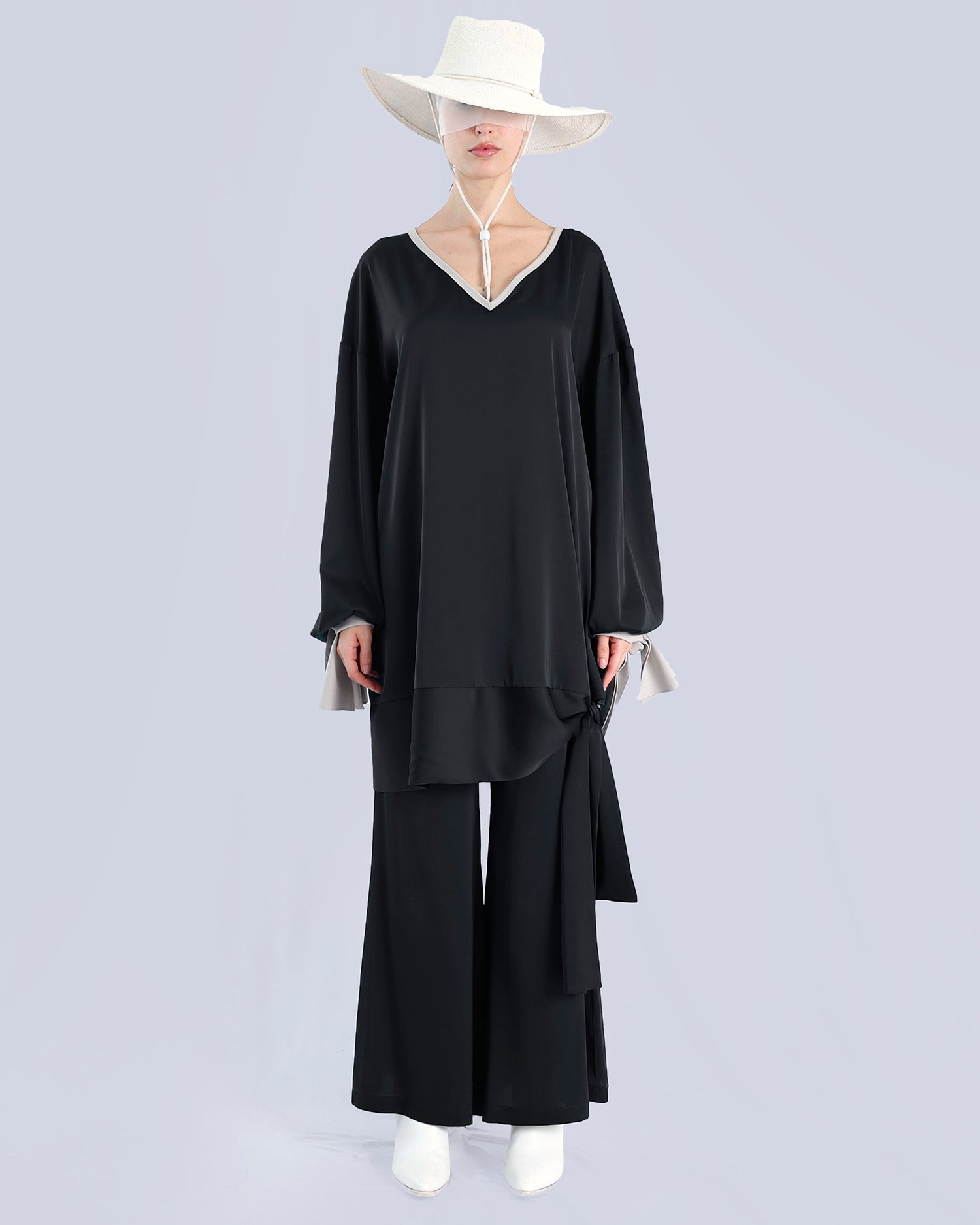 Person wearing a black outfit with a white hat on a light gray background. Maison Marie Saint Pierre | Tunique | PELLEGRINA | Black-Fog| Pants | PAMELA | Black 