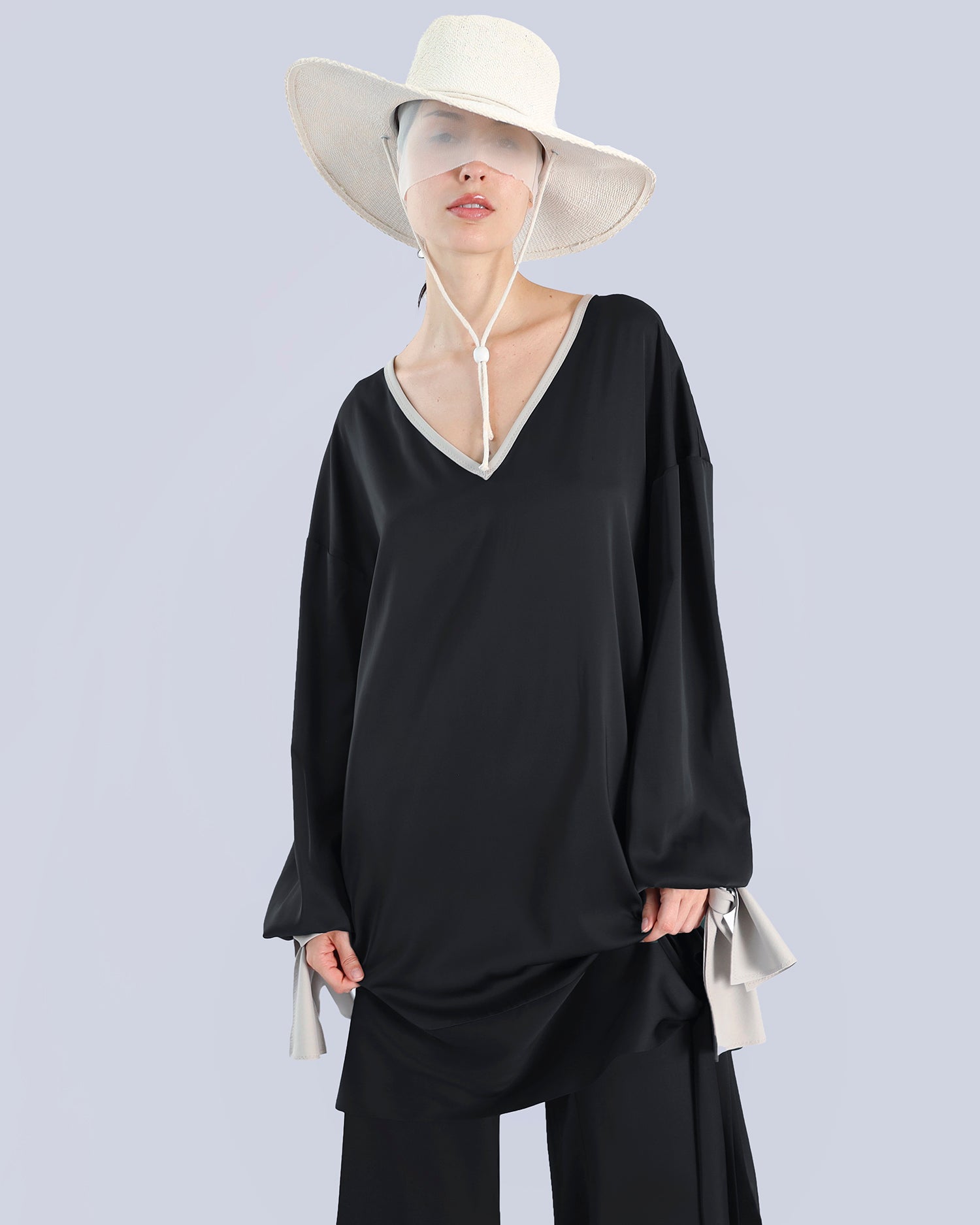 Person wearing a black outfit with a wide-brimmed white hat on a light gray background. Maison Marie Saint Pierre | Tunique | PELLEGRINA | Black-Fog| Pants | PAMELA | Black 