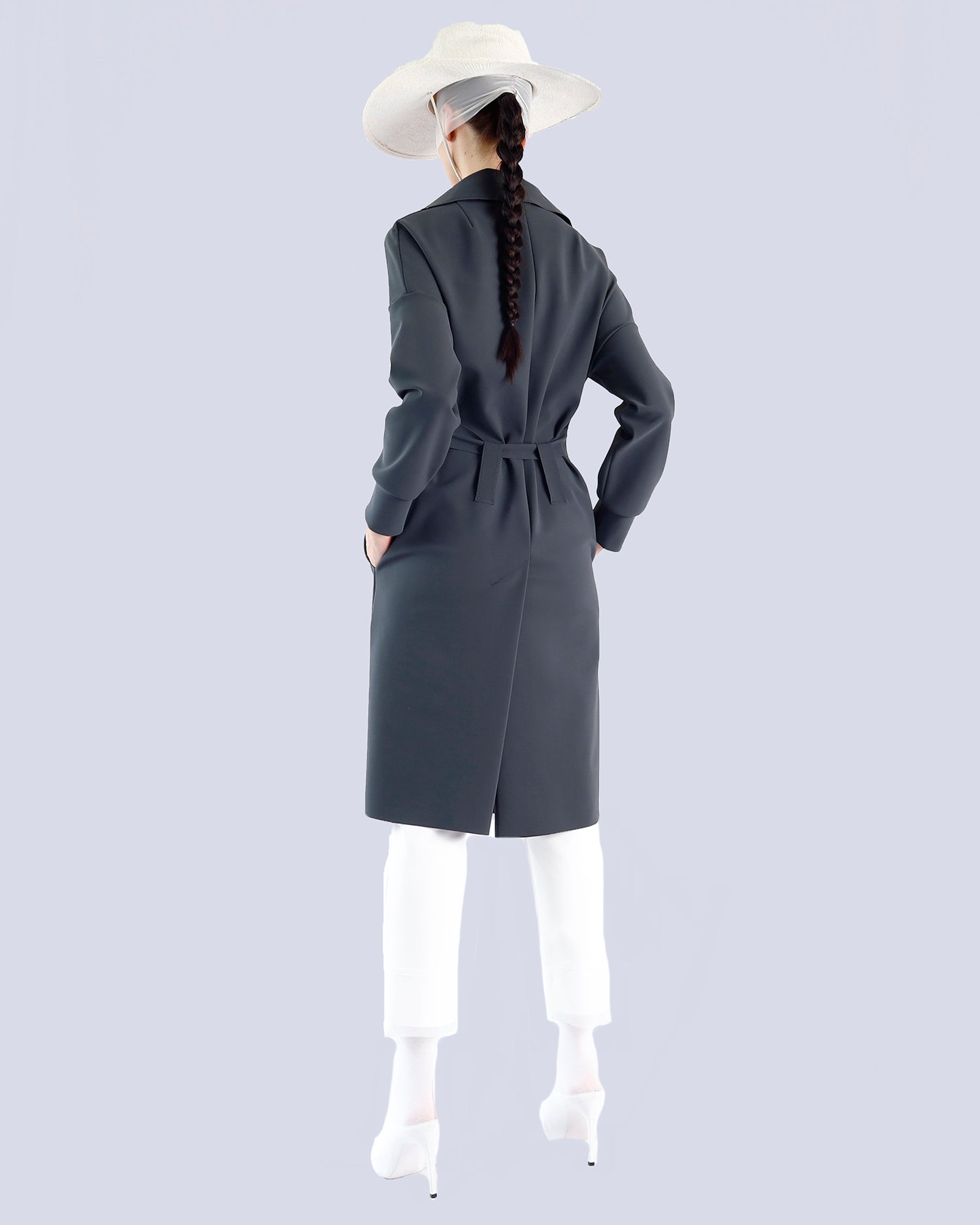 Person wearing a long dark gray coat with a white hat and white pants on a light gray background. Maison Marie Saint Pierre | Coat | PELLINAME | ANT