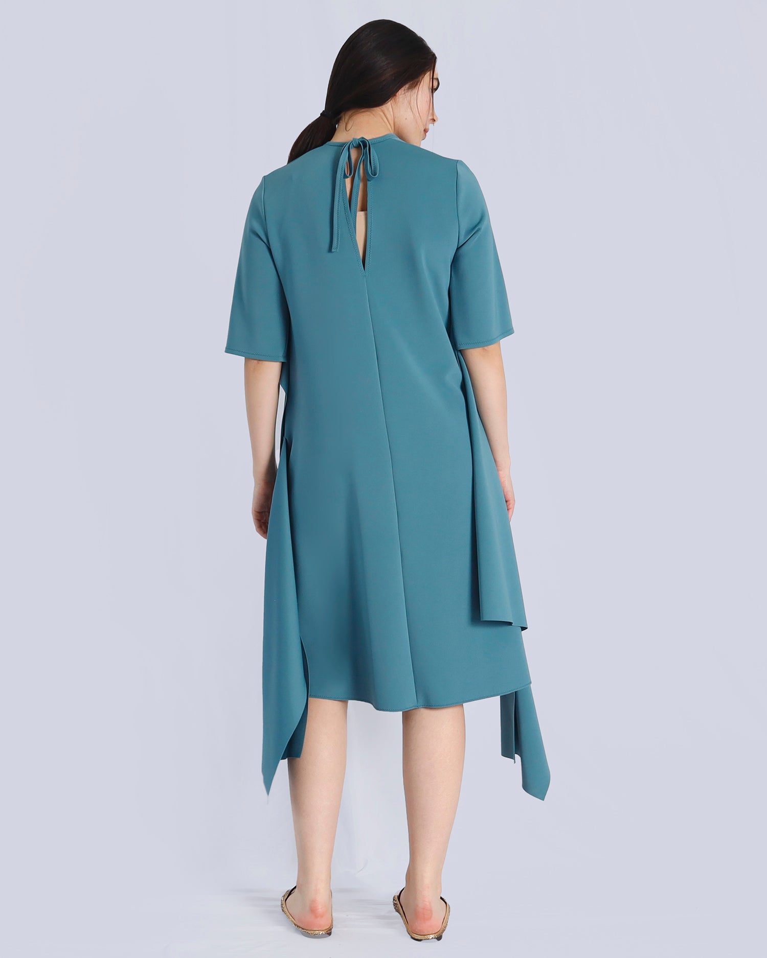 Woman wearing a teal dress with a cutout back on a light gray background. Maison Marie Saint Pierre | Dress | PRISCA | Conifer