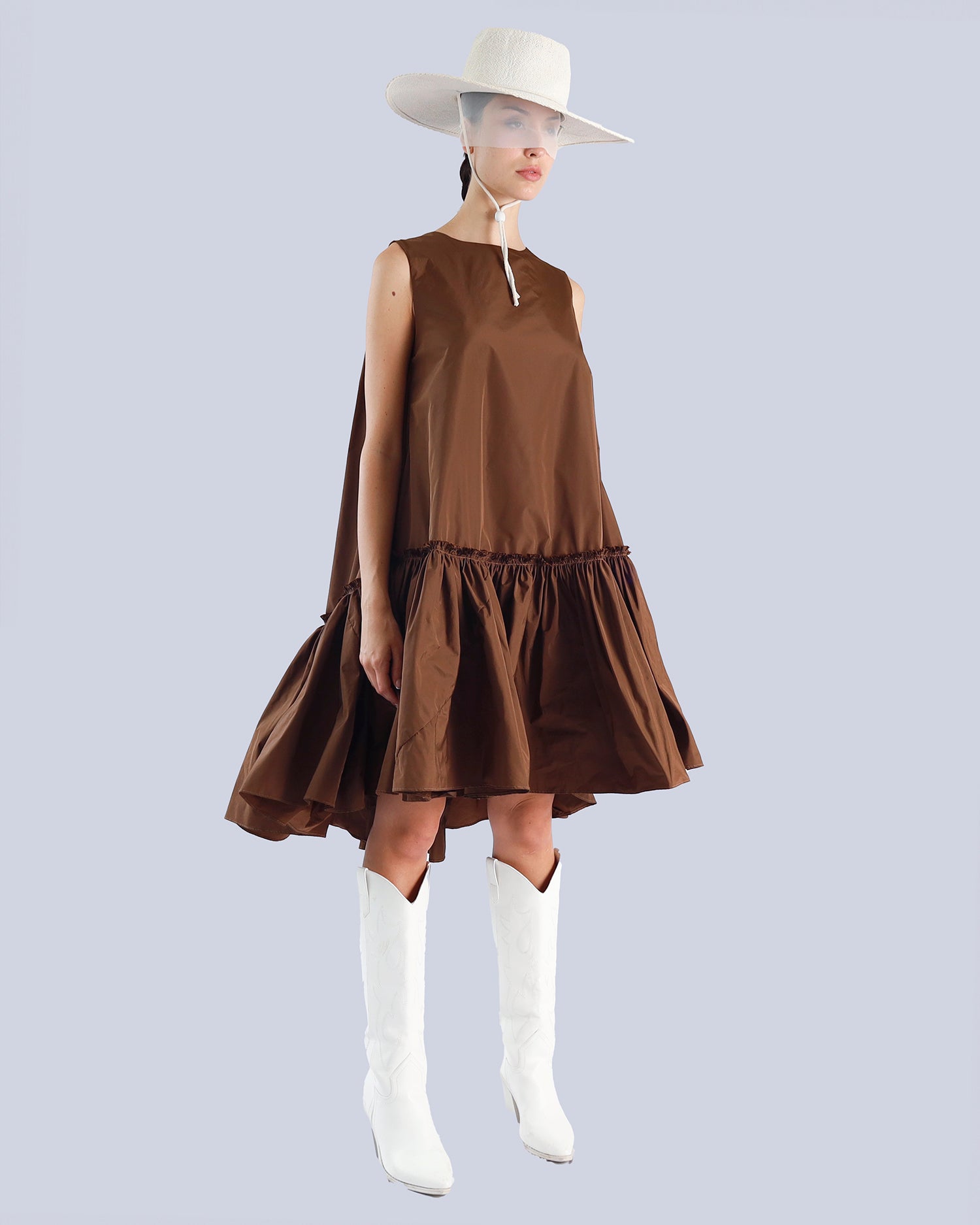 Woman wearing a brown dress with a white hat and white boots on a light purple background. Maison Marie Saint Pierre | Dress | PENSEE |  Dark Umber 