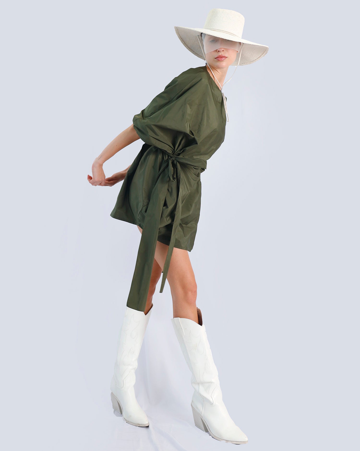 Person wearing a green dress with a tie waist, white boots, and a wide-brimmed hat on a light gray background. Maison Marie Saint Pierre | Dress | PHAENNE |  Kaki